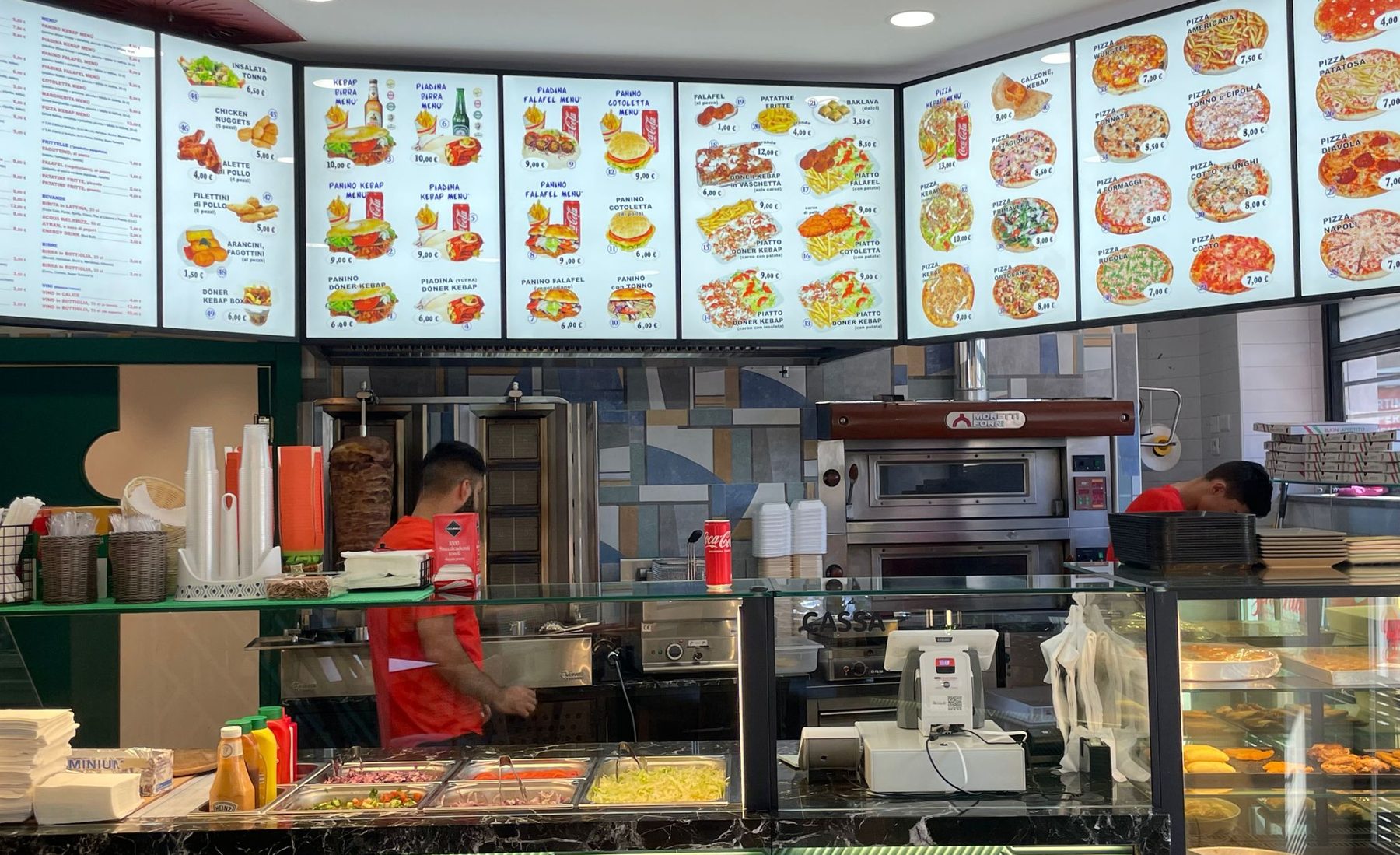 Il banco del locale: le lavagne luminose del menù, lo spiedo del döner e il forno per la pizza.